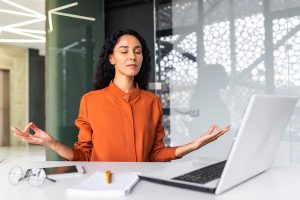 Come ridurre il rumore in ufficio: donna che medita di fronte al suo PC